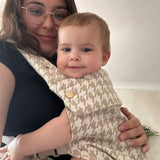 Woman holding a baby wrapped in a patterned blanket indoors.