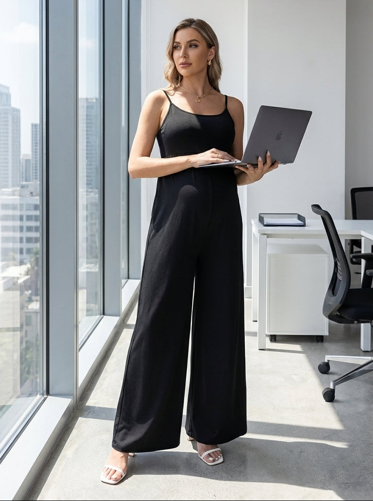Woman in a black jumpsuit holding a laptop in a modern office setting.
