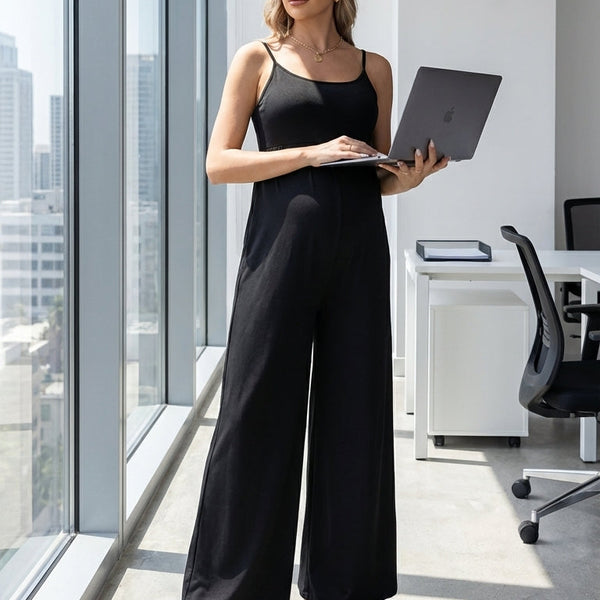 Woman in a black jumpsuit holding a laptop in a modern office setting.