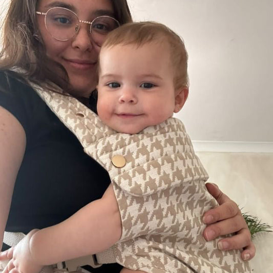 Woman holding a baby wrapped in a patterned blanket indoors.