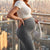 Woman standing on a balcony with a cityscape view during sunset.